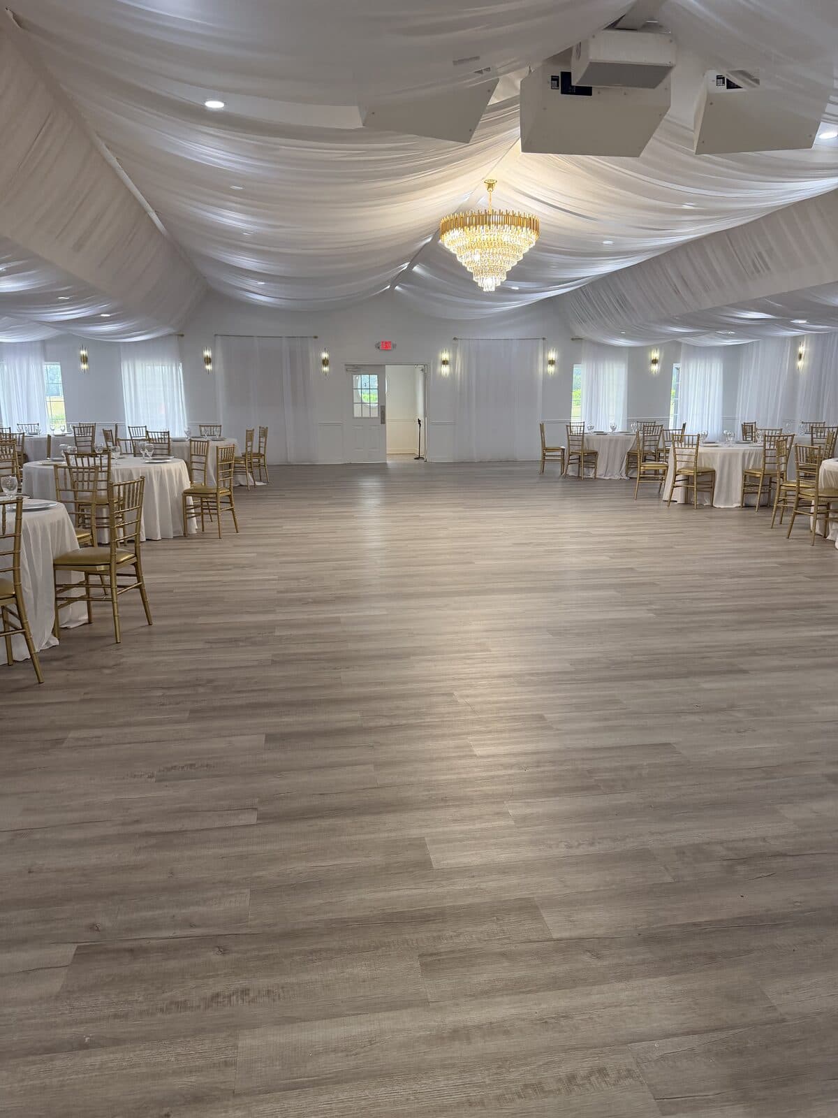 Open hardwood-look dance floor beneath a grand crystal chandelier and draped ceiling